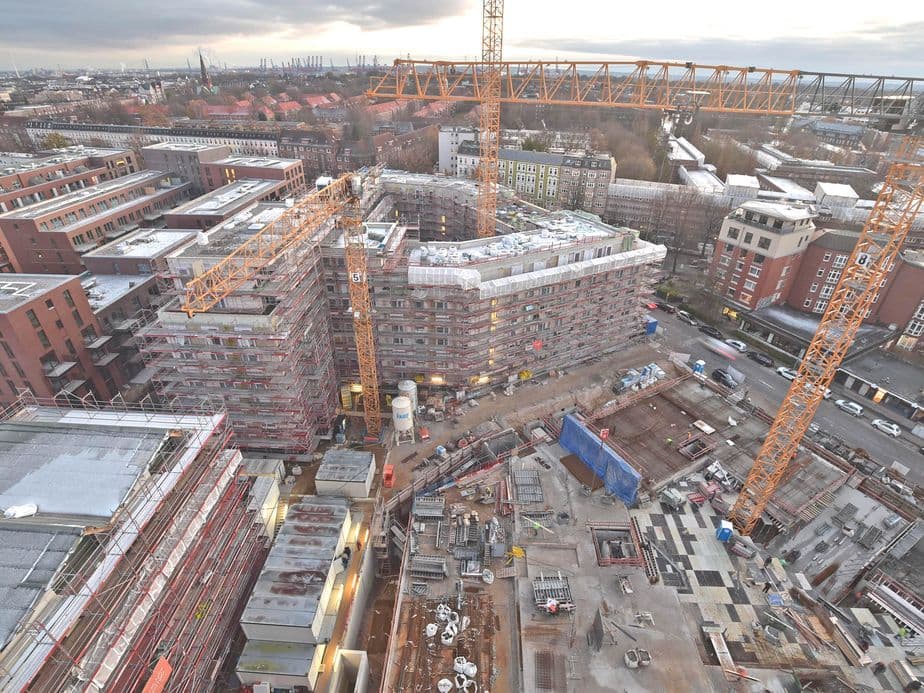 Aerial view of a large construction site with cranes, scaffolding, and partially built structures in an urban area.