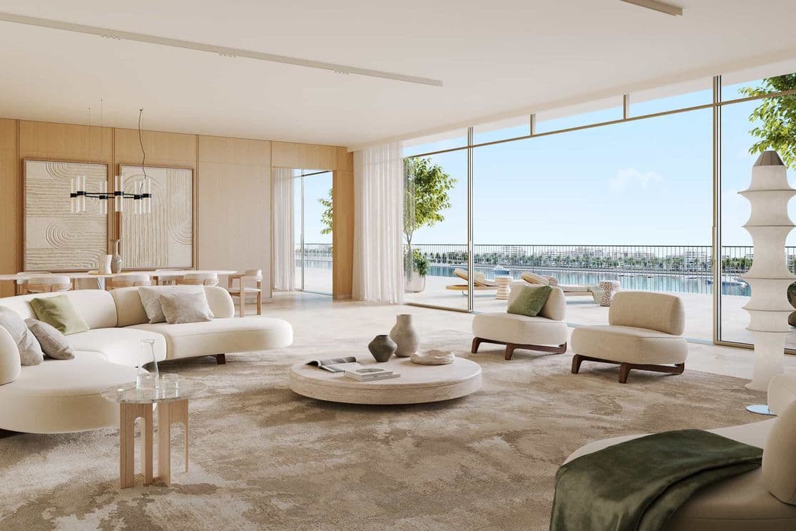 Geräumiges, modernes Wohnzimmer mit weißen Sofas, großen Fenstern und Blick auf einen Balkon mit Blick aufs Wasser. Neutrale Töne und minimalistisches Dekor.