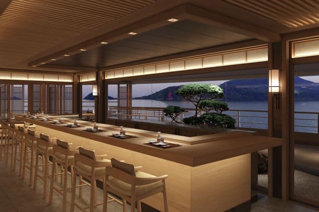 Ein Speisesaal im japanischen Stil mit einer langen Holztheke und Hockern, warmer Laternenbeleuchtung, Shoji-Wänden und einem Meerblick auf die fernen Hügel und Bonsai-Bäume.