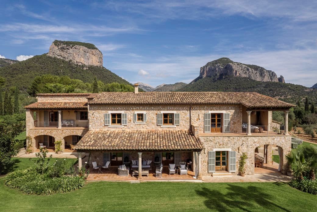 Vista aérea de la finca "Turmalina" en Alaró, Mallorca, que muestra la casa principal rodeada de exuberantes jardines, una amplia piscina y el imponente telón de fondo de las montañas de la Tramuntana.