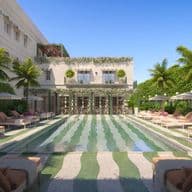 Lujosa zona de piscina al aire libre con azulejos a rayas, rodeada de tumbonas, sombrillas, palmeras y un edificio adornado con vegetación.