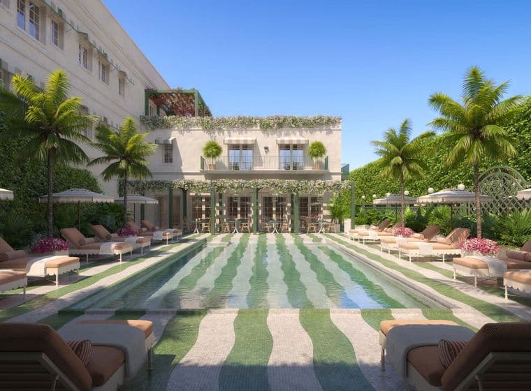 Luxurious outdoor pool area with striped tiles, surrounded by lounge chairs, umbrellas, palm trees, and a building adorned with greenery.