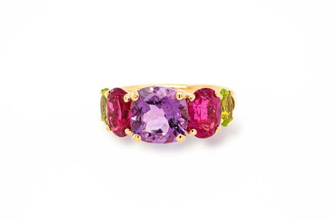 A gold ring with a large purple gemstone flanked by pink and green gemstones.