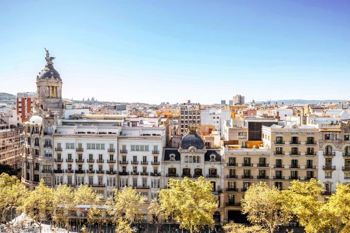 Paisatge urbà de Barcelona amb edificis ornamentats, arbres daurats i un cel blau clar.