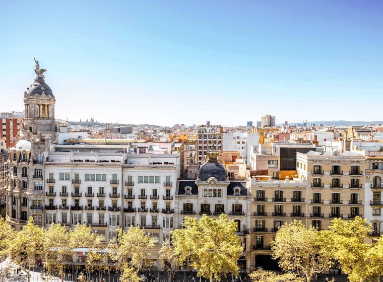 Paisatge urbà de Barcelona amb edificis ornamentats, arbres daurats i un cel blau clar.
