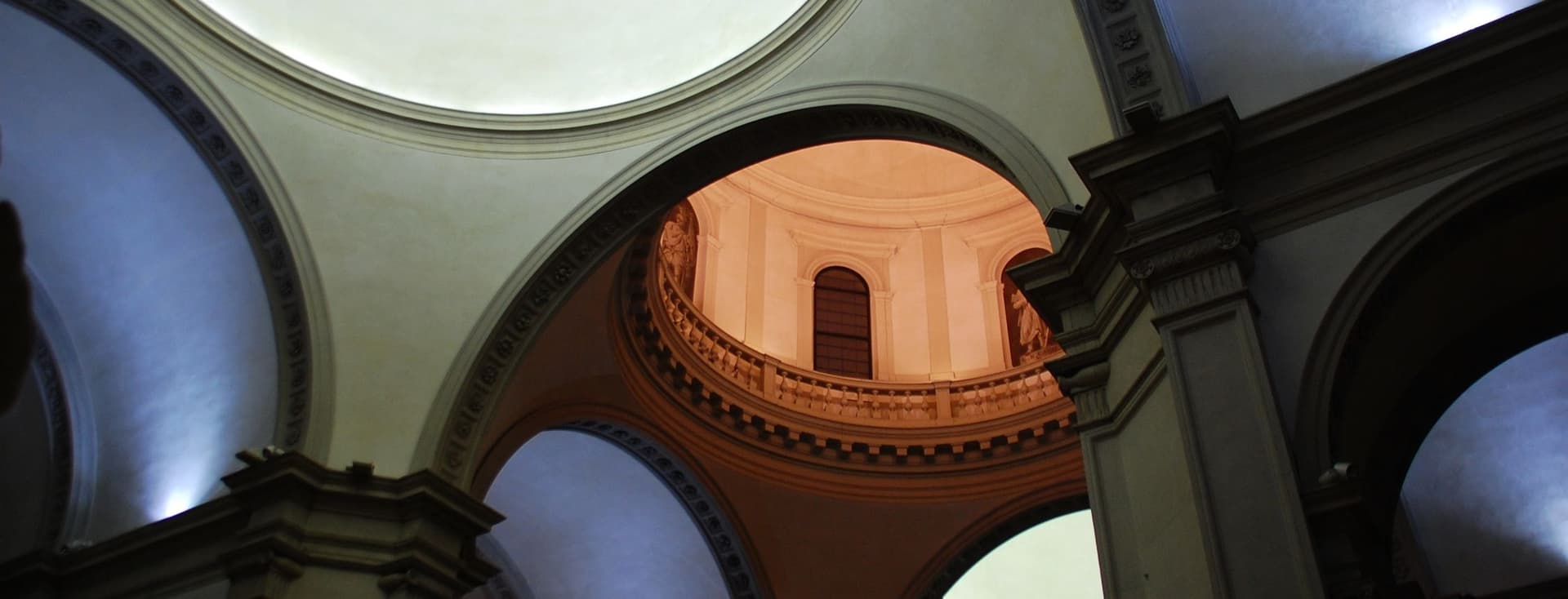 Innenansicht einer historischen Kirche oder Kathedrale, die dramatische architektonische Elemente zeigt, darunter mehrere Kuppeln, Bogengänge und eine warm beleuchtete kreisförmige obere Kammer mit Balustrade. Der Raum verfügt über klassische Steinsäulen und dramatische Beleuchtung.WiederholenClaude kann Fehler machen. Bitte überprüfen Sie die Antworten.