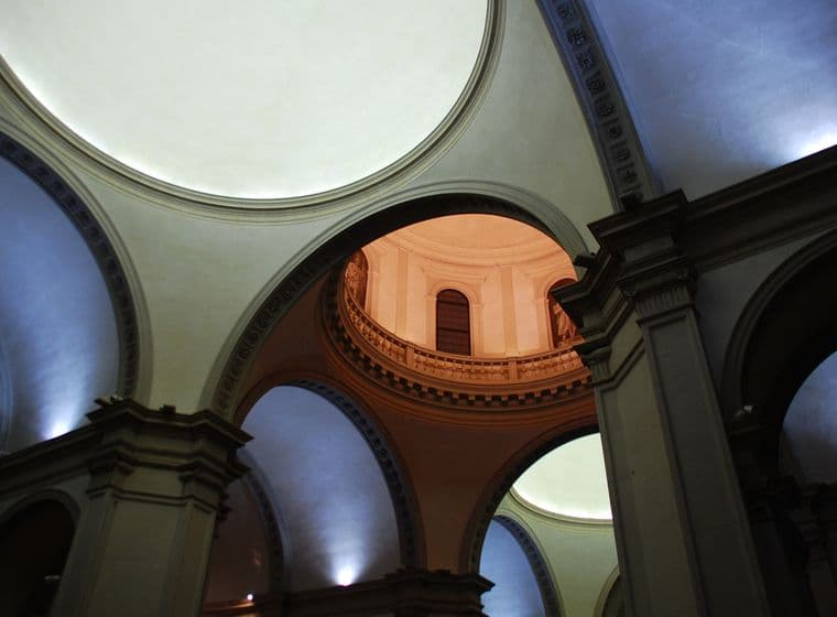 Innenansicht einer historischen Kirche oder Kathedrale, die dramatische architektonische Elemente zeigt, darunter mehrere Kuppeln, Bogengänge und eine warm beleuchtete kreisförmige obere Kammer mit Balustrade. Der Raum verfügt über klassische Steinsäulen und dramatische Beleuchtung.WiederholenClaude kann Fehler machen. Bitte überprüfen Sie die Antworten.