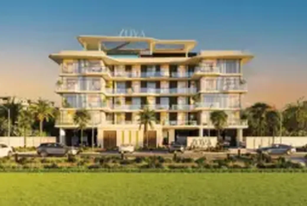 Modern multi-story building with glass balconies, surrounded by palm trees and parked cars, set against a blue sky and green lawn.