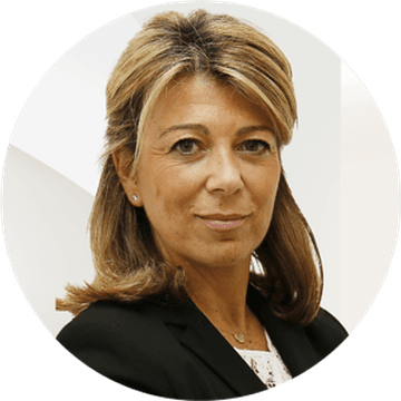 Portrait d'une femme souriante aux cheveux blonds, portant un blazer noir et un haut en dentelle blanche.