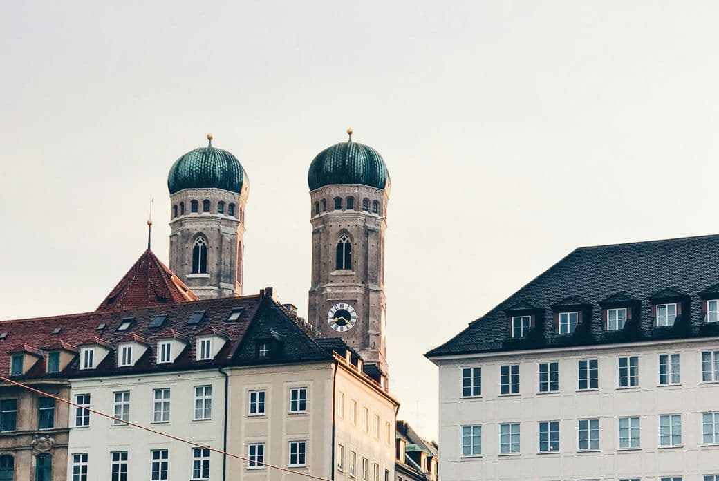 Rooftop view of Munich with the twin domes of Frauenkirche and surrounding historic buildings under a clear sky.