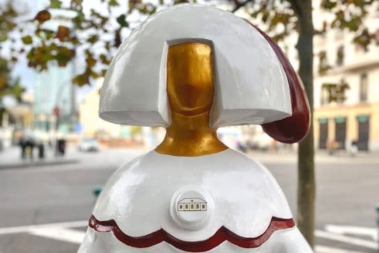 Una estàtua blanca d'una dona amb la cara daurada i claus al vestit es troba en una plaça de la ciutat.