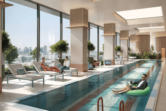 Luxurious indoor pool area with oversized glass walls, mosaic-clad columns, lounge chairs, greenery, and people relaxing by the water.