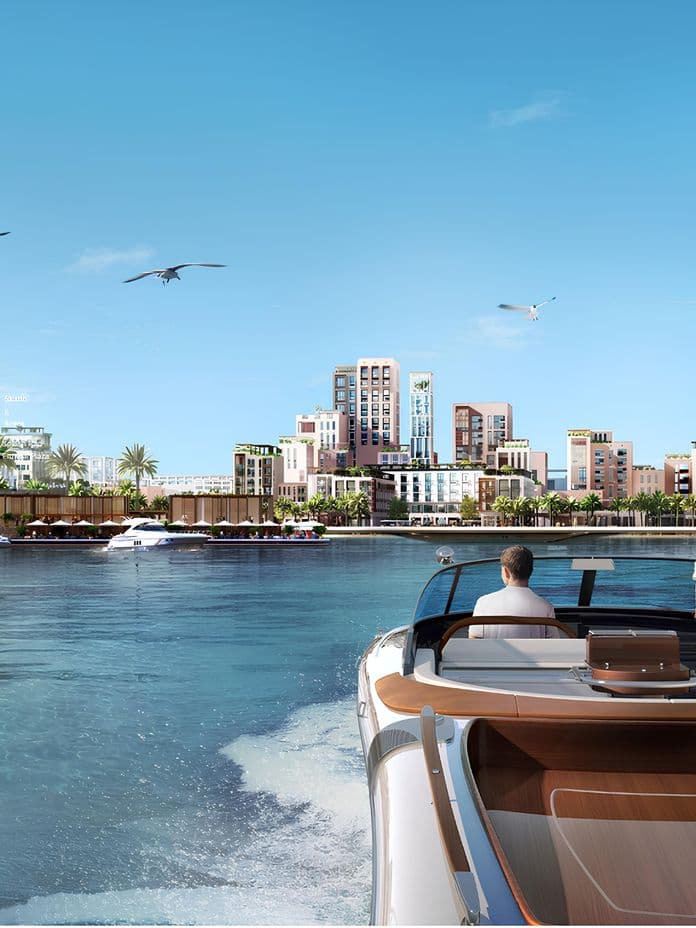 A couple on a boat ride in a sunny marina, surrounded by modern buildings, palm trees, and seagulls flying in a clear blue sky.