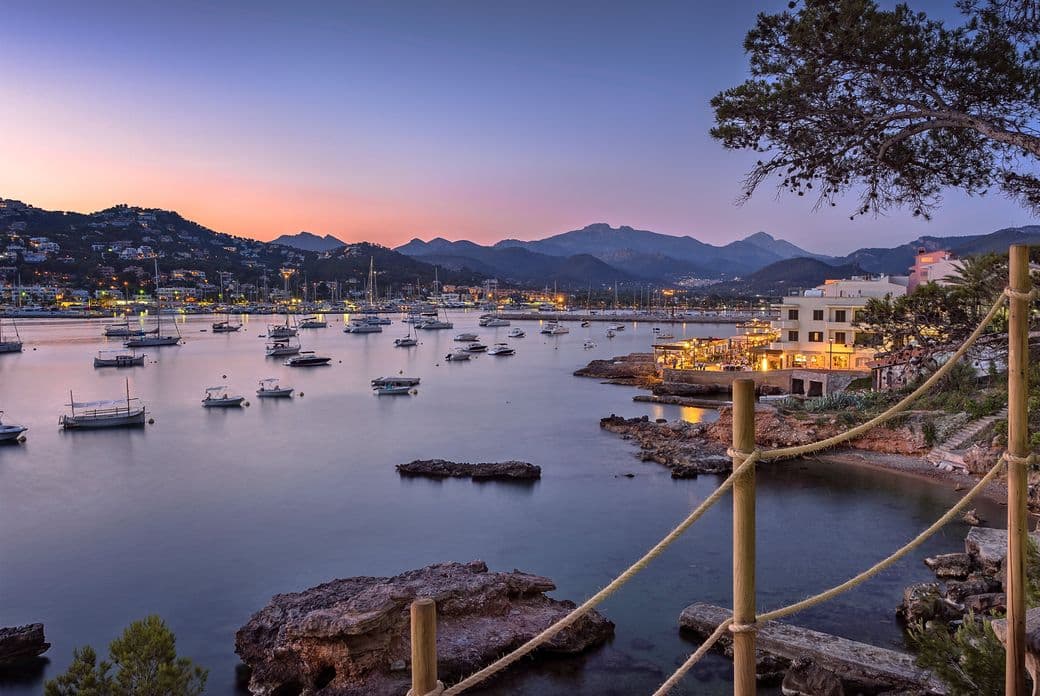 Sonnenuntergangsblick auf den Hafen von Port Andratx im Südwesten Mallorcas, mit Booten und einem bunten Himmel, der sich im Wasser spiegelt.