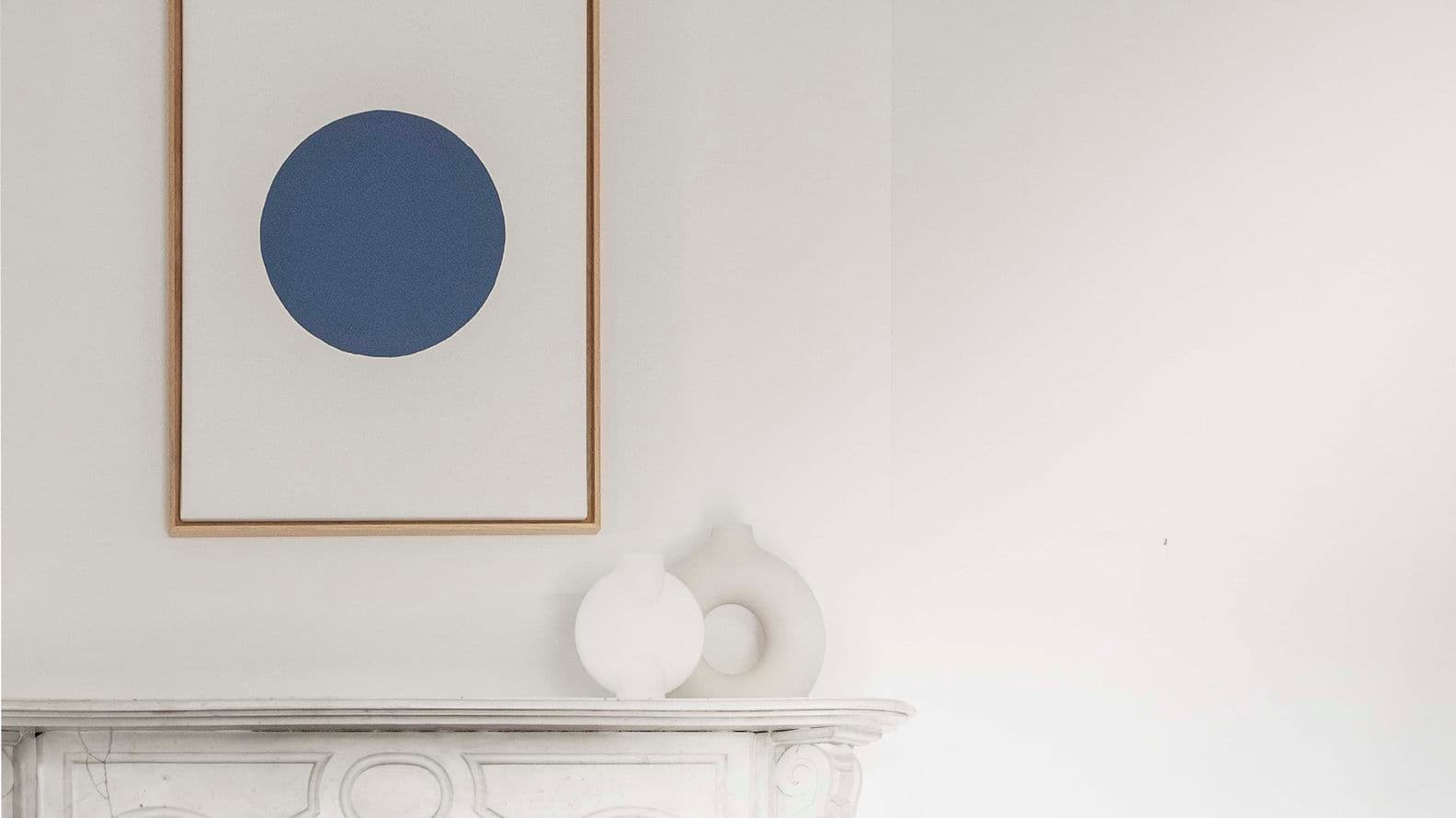 Minimalistisches Zimmer mit einem weißen Marmorkamin und einem gerahmten Kunstwerk mit einem großen blauen Kreis auf weißem Hintergrund darüber.