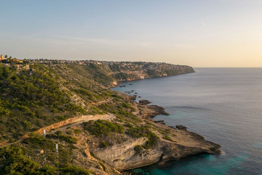 Vista aèria de la costa agresta i el camí de penya-segat a Puig de Ros, Mallorca, amb vistes al mar durant la posta de sol.