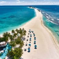 Luftaufnahme einer tropischen Insel mit weißem Sand, türkisfarbenem Wasser, Palmen, Sonnenschirmen und einem Resort.
