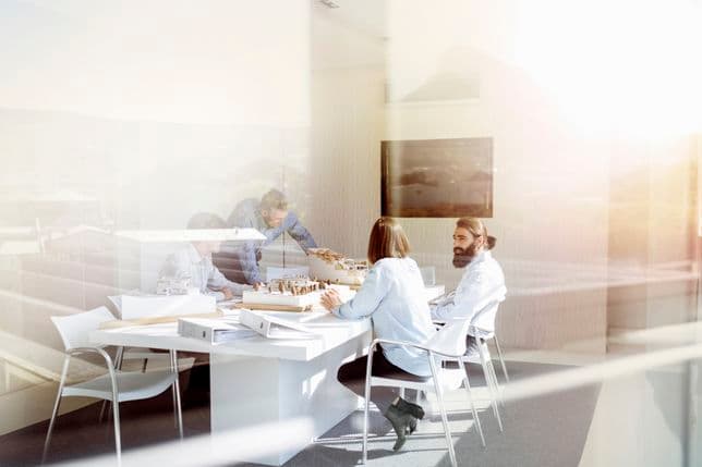 Eine Gruppe von Menschen in einem hellen Büro arbeitet gemeinsam an einem Tisch mit Architekturmodellen und Dokumenten.