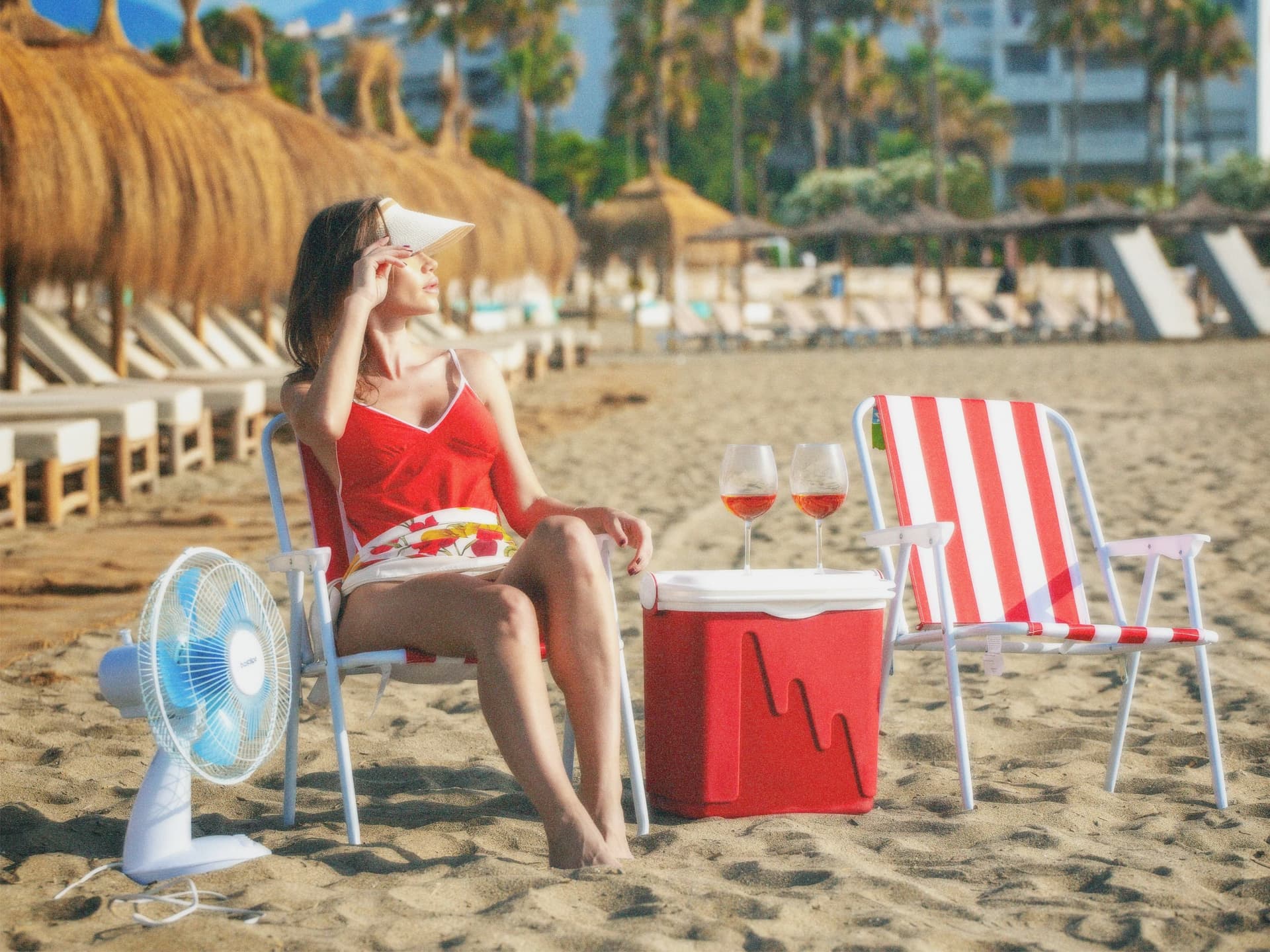 Bild einer Frau am Strand in Rottönen. Auf einem Stuhl sitzend und mit einem Ventilator.