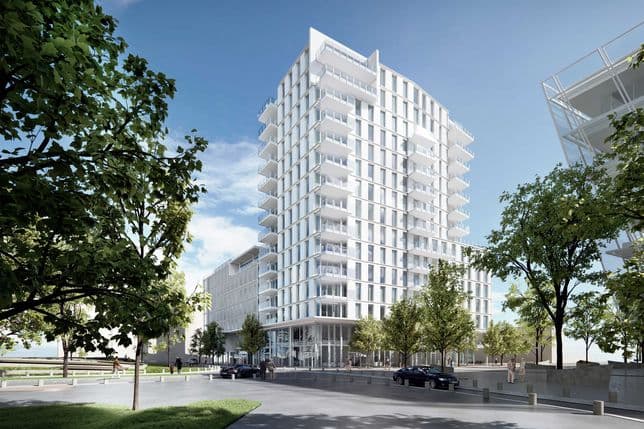 Modern white high-rise building with balconies, surrounded by trees and cars on a sunny day.