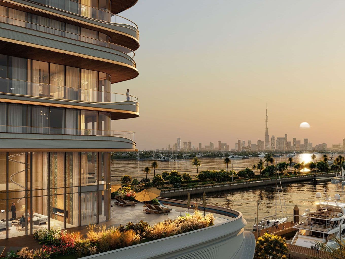 Curved modern building with balconies overlooking a marina and city skyline at sunset, featuring yachts and lush greenery.