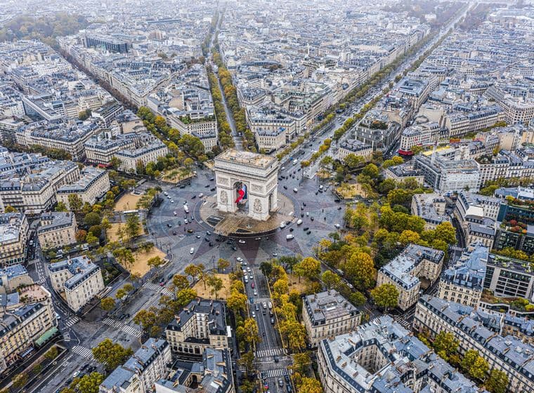 Vue aérienne de Paris, en France, avec l'Arc de Triomphe au centre d'un réseau d'avenues en étoile. Des bâtiments et des arbres bordent les avenues.