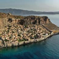Aerial view of Monemvasia, Greece, a medieval town on a rocky island, surrounded by turquoise sea and mountains.
