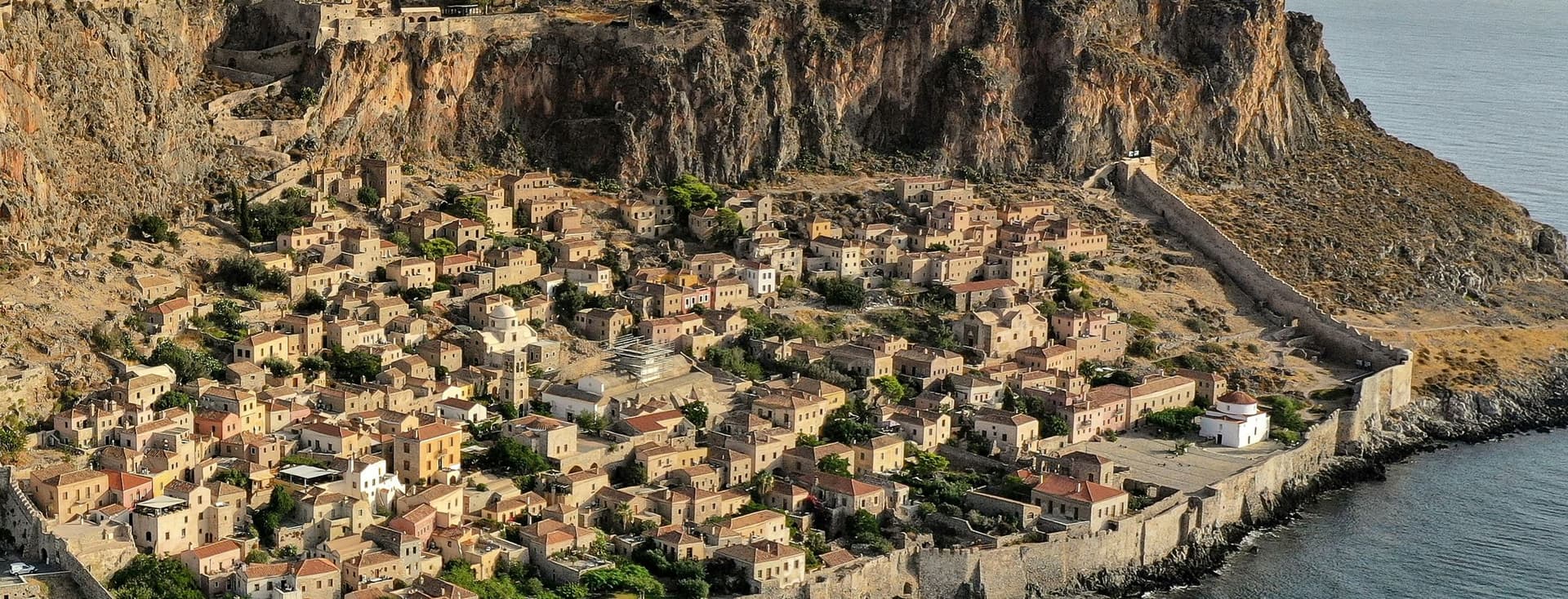 Aerial view of Monemvasia, Greece, a medieval town on a rocky island, surrounded by turquoise sea and mountains.