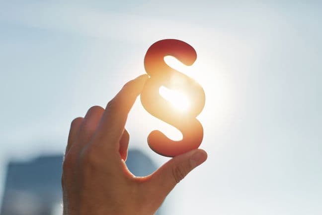 Hand silhouetted against a bright sky holding up a paragraph symbol with sun shining through, creating a backlit effect