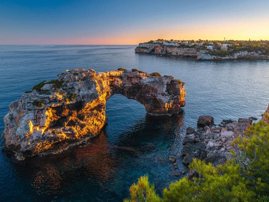 Drone view of Es Pontàs, the stunning natural rock arch rising from the Mediterranean Sea off the southeast coast of Mallorca, surrounded by crystal-clear waters and dramatic cliffs