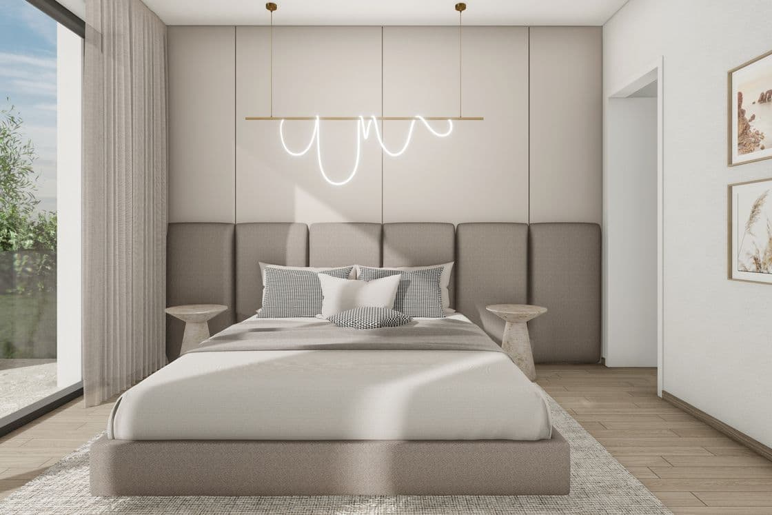 Modern bedroom with an upholstered headboard, pendant designer light, light-colored textiles, and a view through a large window onto a terrace with greenery.