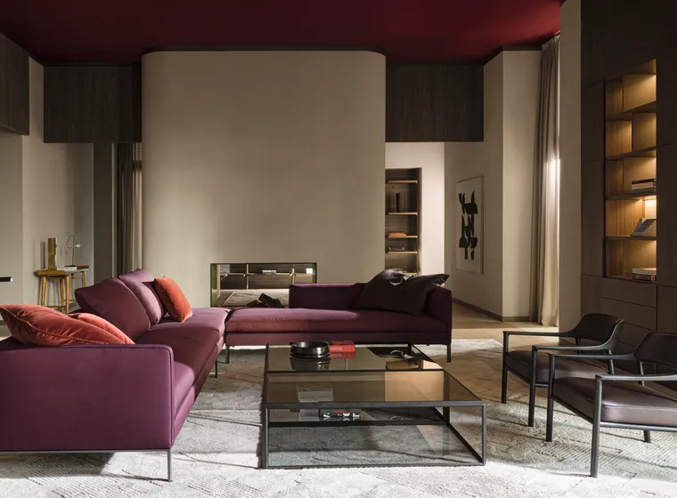Modern living room with a purple sectional sofa, glass coffee table, dark wood built-ins, backlit shelves, and a curved beige fireplace wall.