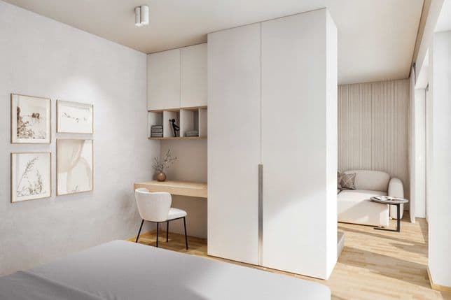 Bright bedroom with a small desk area, built-in cabinets, and a view into the living space, featuring minimalist design in natural tones.