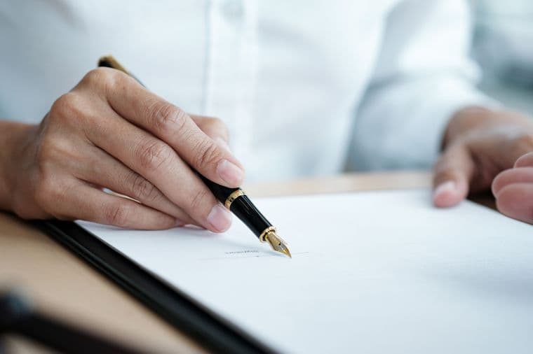Une personne signe un document avec un stylo plume noir et doré sur un presse-papiers noir.