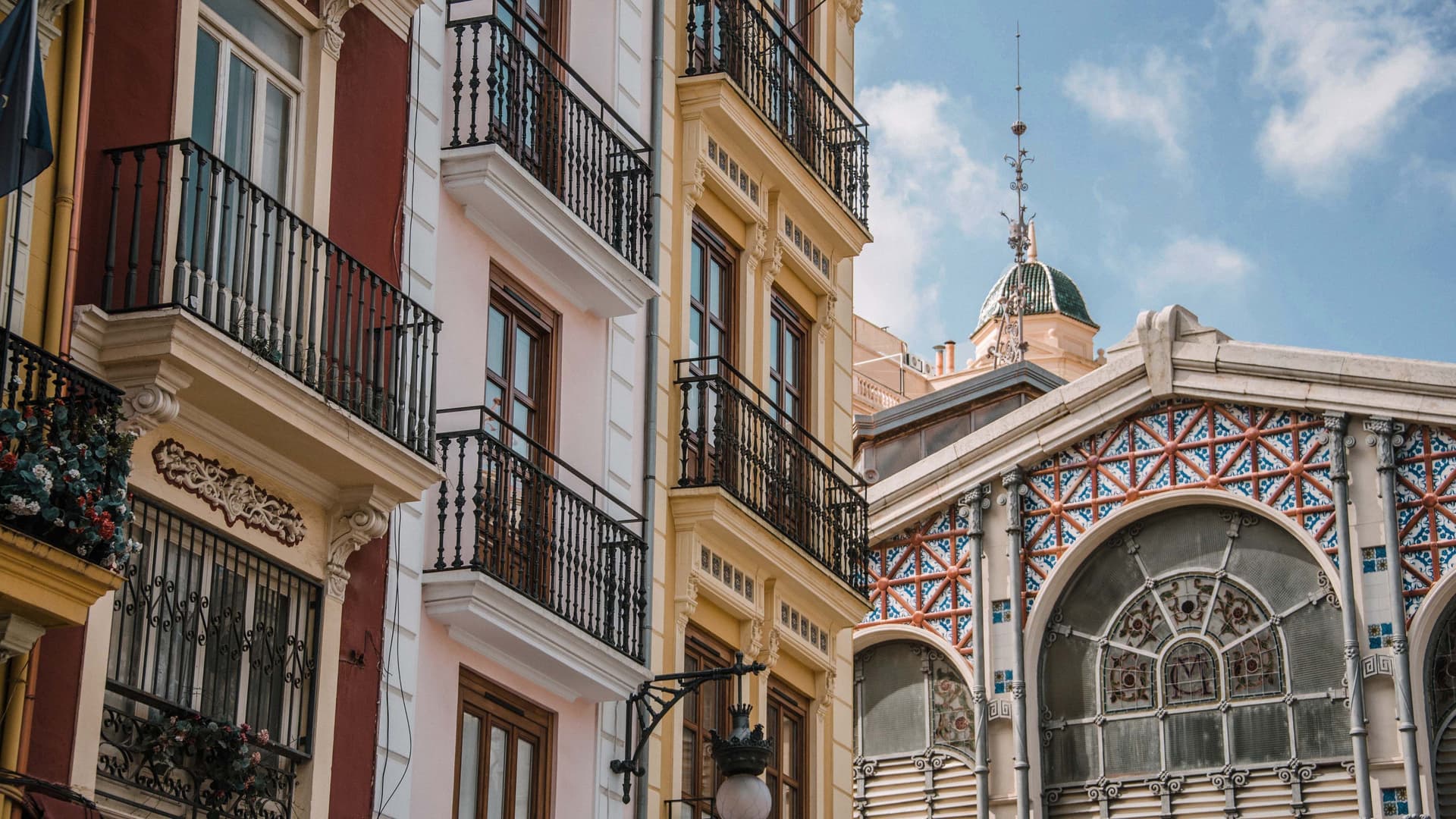 Vista exterior d'edificis colorits amb balcons i un mercat amb una cúpula verda a València, Espanya.