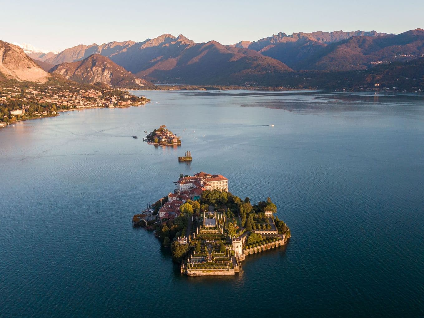 Immagine aerea del Lago Maggiore: acque azzurre che si estendono tutt’intorno e un’isola verdeggiante al centro.