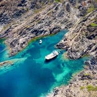 Turquoise blue sea with a rugged coastline and three boats in the coves of Empuriabrava.