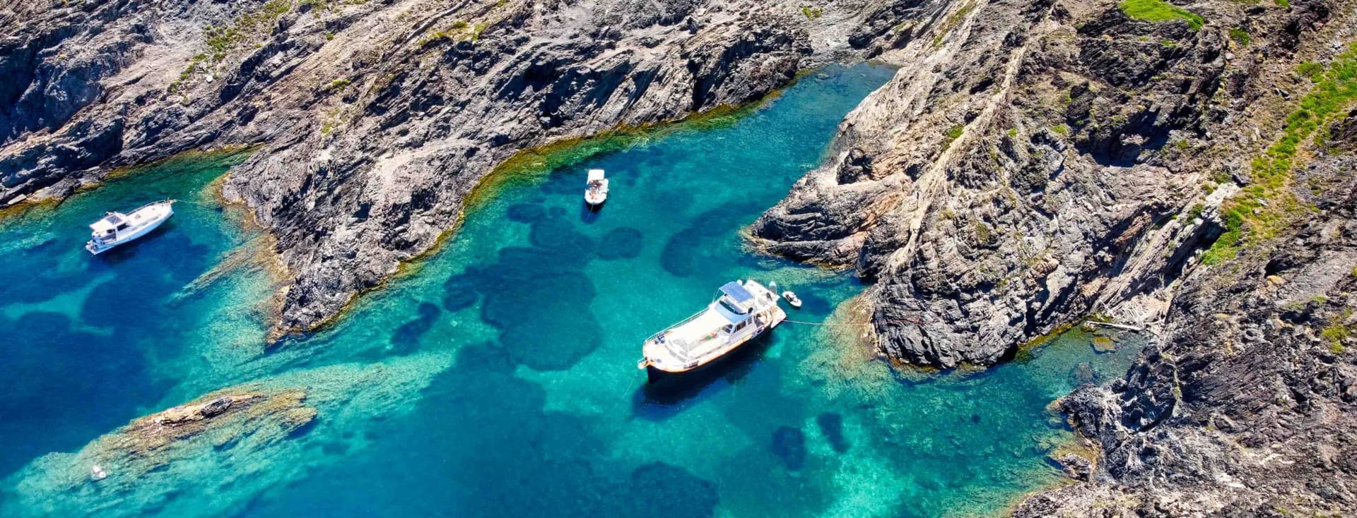Türkisblaues Meer mit einer zerklüfteten Küste und drei Booten in den Buchten von Empuriabrava