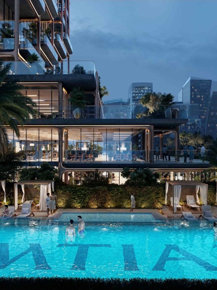 Evening pool at The Symphony by Imtiaz with illuminated turquoise water, palms, cabanas and a modern glass high-rise with city skyline in the background