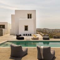 Luxury villa with a pool and bean bag chairs. White building with windows, and a view of the landscape.