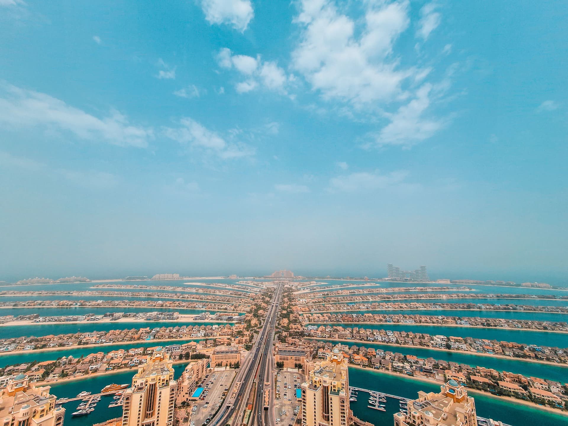 Luftaufnahme der Palm Jumeirah in Dubai mit ihrer markanten palmförmigen Struktur, umgeben von Wohnbereichen und Wasserwegen unter klarem Himmel.