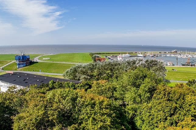 Aerial view of Norddeich, a new development project on the North Sea coast. Trees, the harbor, and the North Sea are visible.