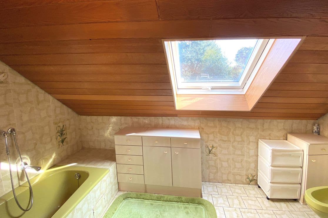 1970s bathroom with green bathtub, wooden ceiling, and skylight in the attic