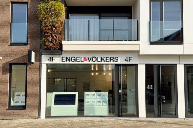 Street view of an Engel & Völkers real estate office with modern facade, large windows, and green wall accents.