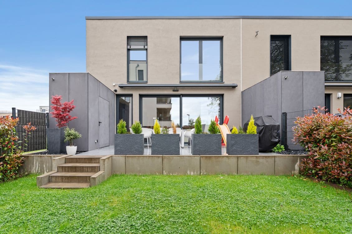 Sand coloured house featuring a terrace with potted plants and a garden with green grass