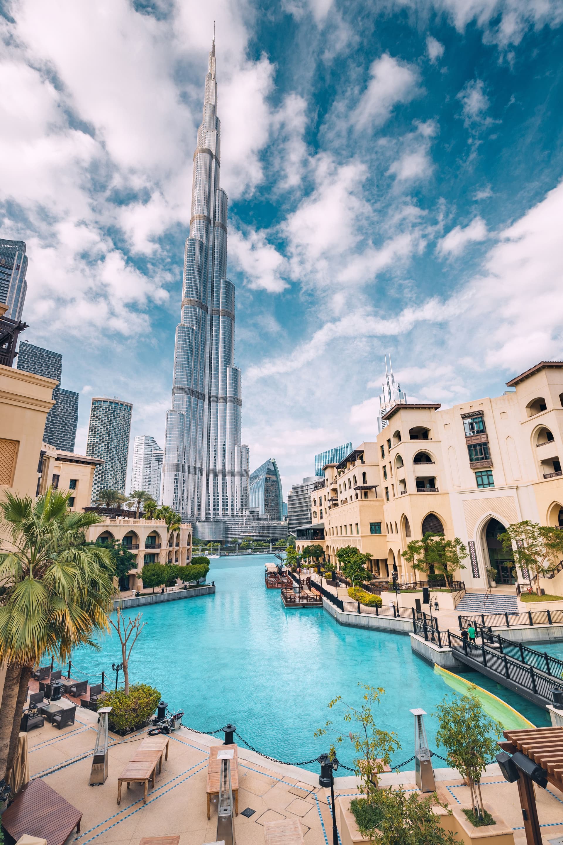 Burj Khalifa skyline view in Downtown Dubai with waterfront promenade, turquoise canals, and modern residential buildings on a sunny day.