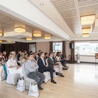 Ein Immobilienmakler präsentiert vor einem sitzenden Publikum in einem hellen Raum mit Engel & Völkers Tragetaschen und Logo.