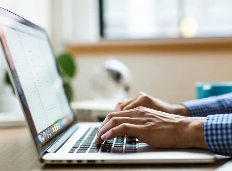 "Person typing on a computer, wearing a checkered shirt, doing real estate marketing."