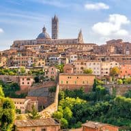 Scenic view of Siena, Italy, showcasing historic buildings and the Siena Cathedral, surrounded by lush greenery under a bright blue sky.