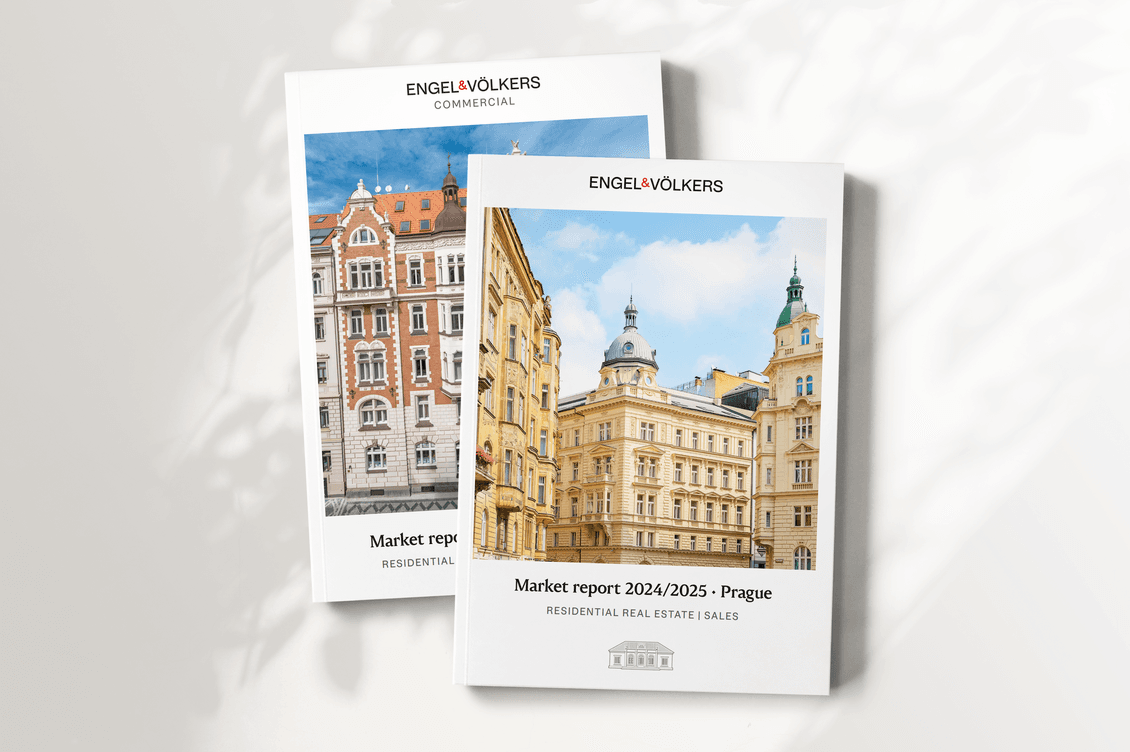 Two Engel & Völkers brochures lying on a white surface. The front cover shows the residential market report with a photo of historic buildings in central Prague under a blue sky. The second, partially hidden, represents the commercial report with another Prague architectural view.